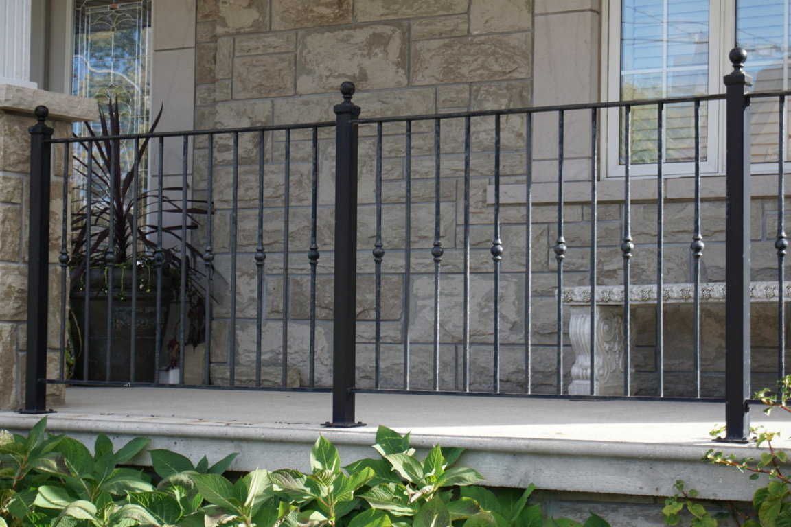 Narrow outdoor space between two buildings, with a wooden fence and shrubbery. A concrete walkway is visible.