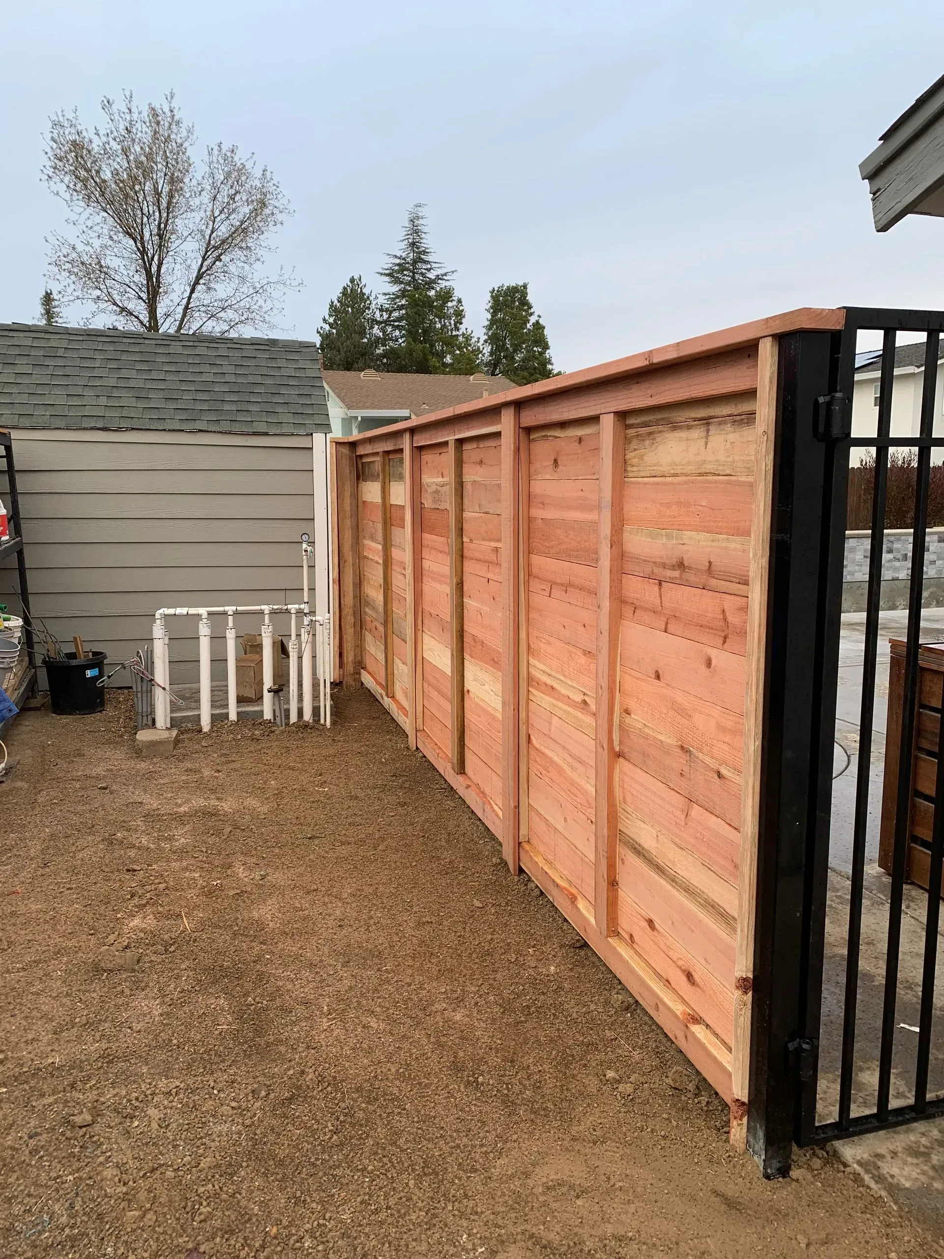 Wooden fence with black metal gate, built next to a gravel-covered yard.