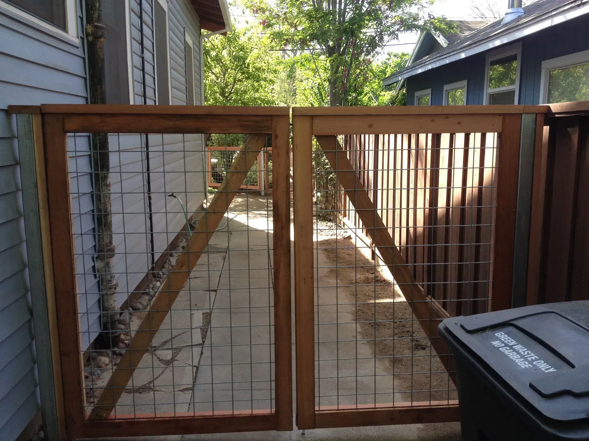 Wooden double gate with wire mesh panels, in a backyard setting.