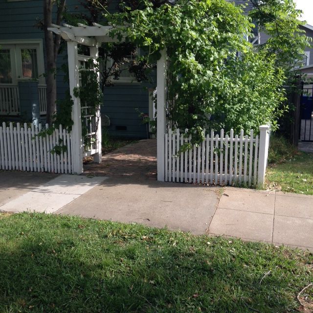 Red wooden privacy fence in front of a house with a gazebo and tile roof on a sunny day.