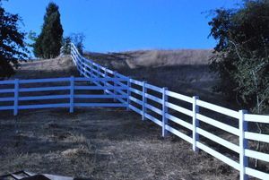White fence on a grassy hill under a bright blue sky.
