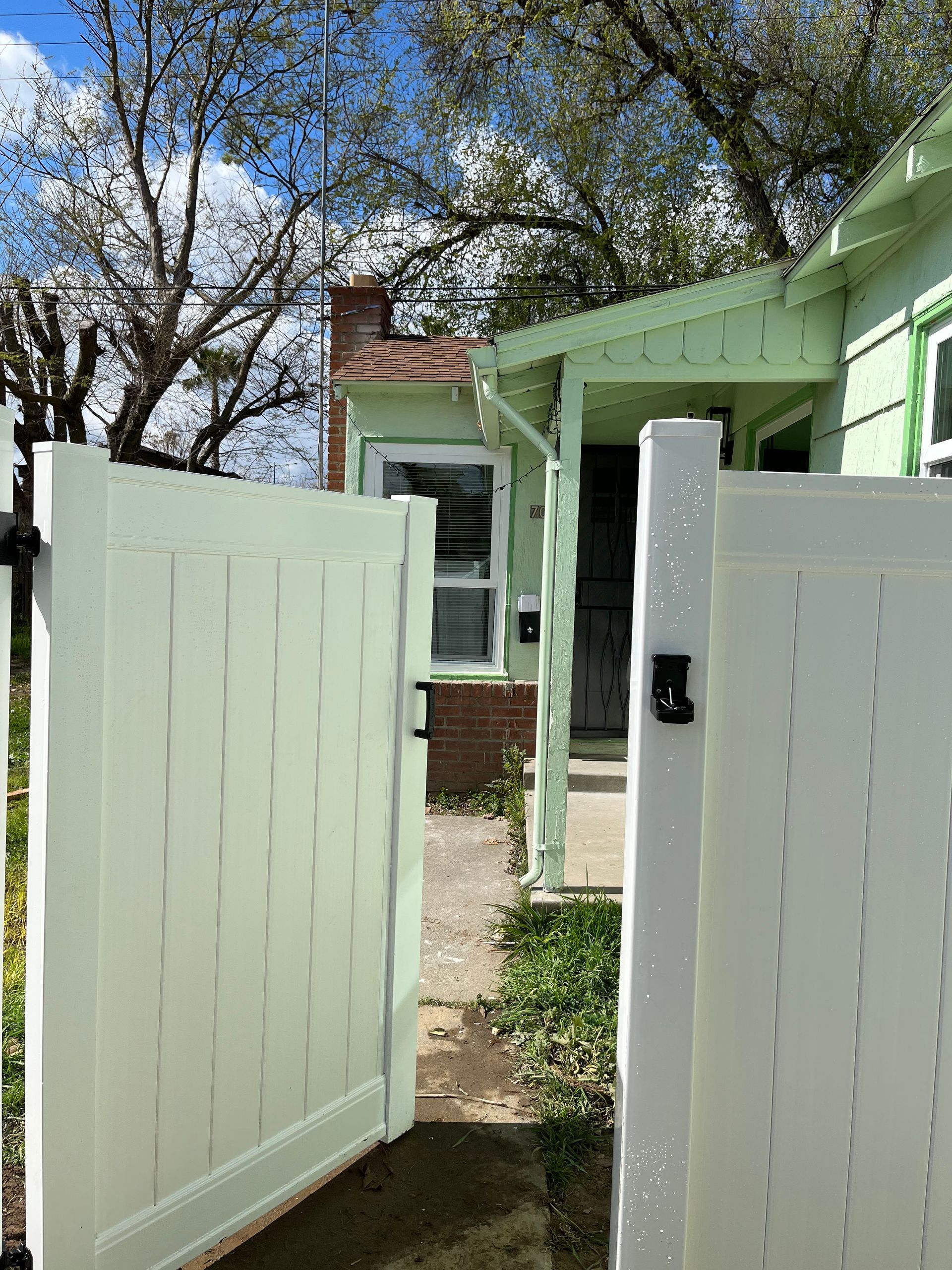 Driveway with a wooden fence, red house, and white garage on a sunny day.