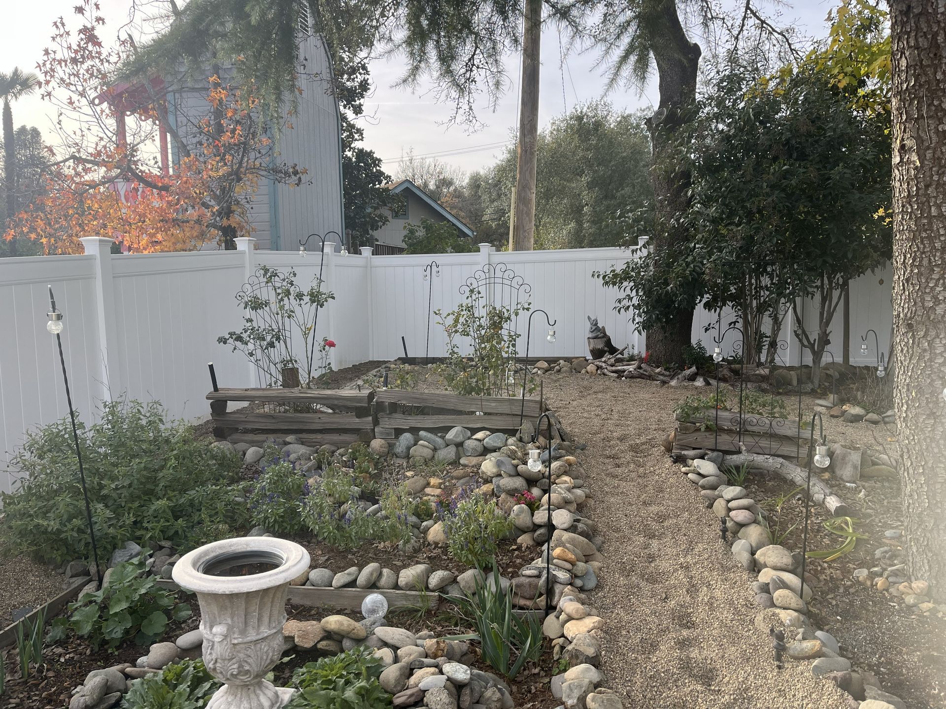 Wooden fence in a backyard with landscaping; brown mulch, green plants, and a partly cloudy sky.