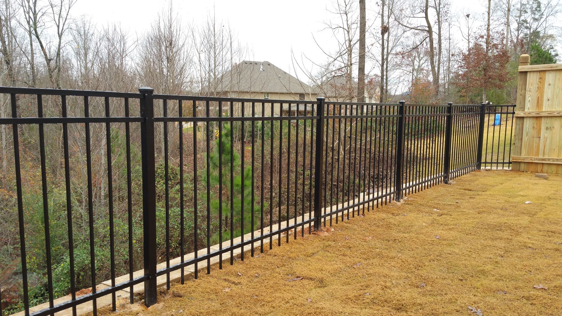 Wooden gate with vertical planks, attached to a wire fence. Set against trees and a cloudy sky.