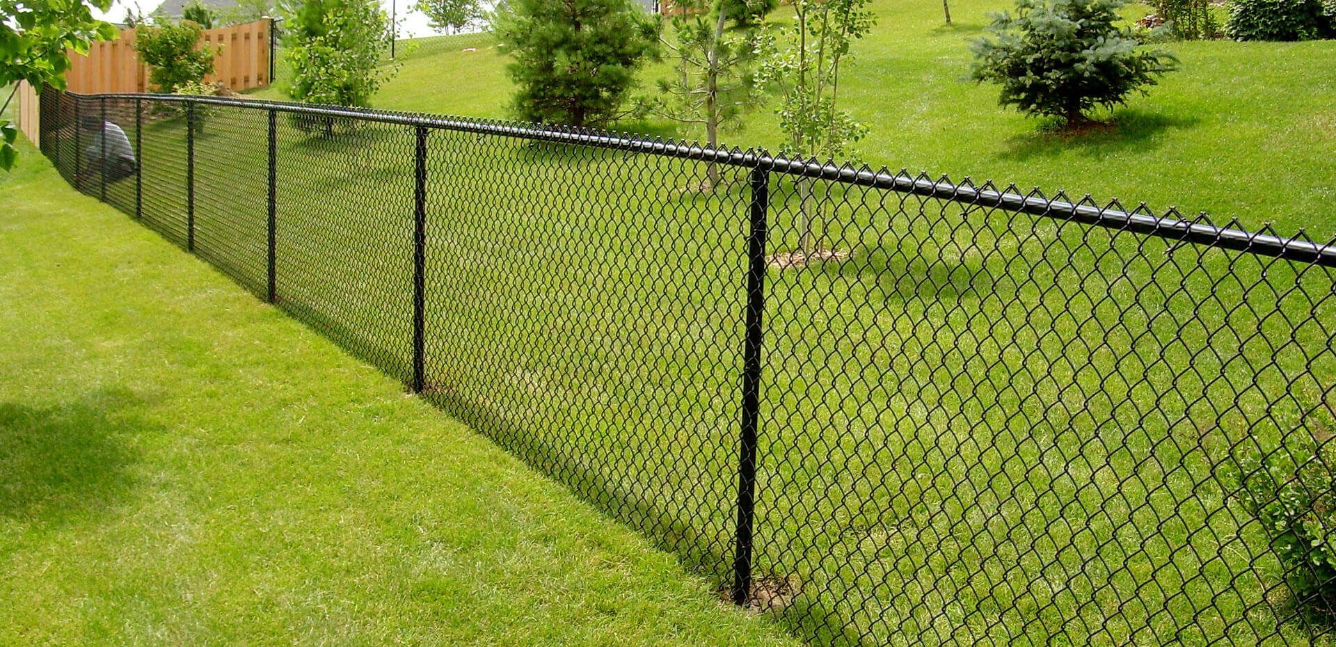 Wooden fence with wire mesh panels, next to a dirt embankment, under trees.