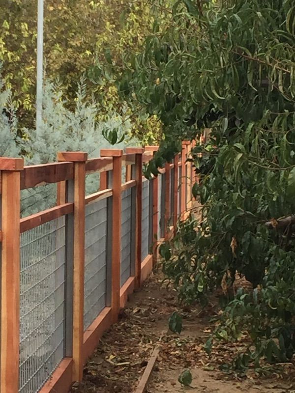 Wooden fence and gate in front of a house, with trees in the background, viewed from inside a vehicle.