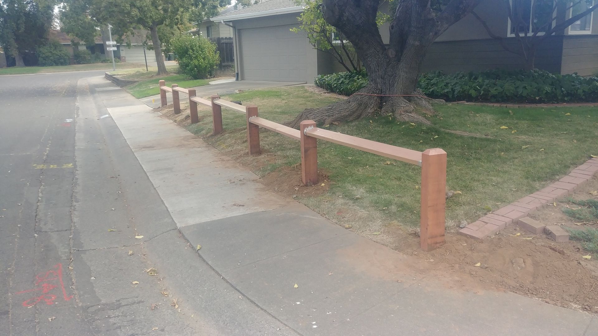 Wooden fence in a yard with mulch and small plants, under a blue sky.