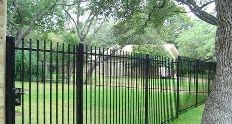 Wooden fence in a backyard with landscaping; brown mulch, shrubs, and blue sky.