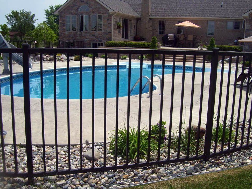 Black metal fence enclosing a patio with French doors, fire pit, and a beige house.