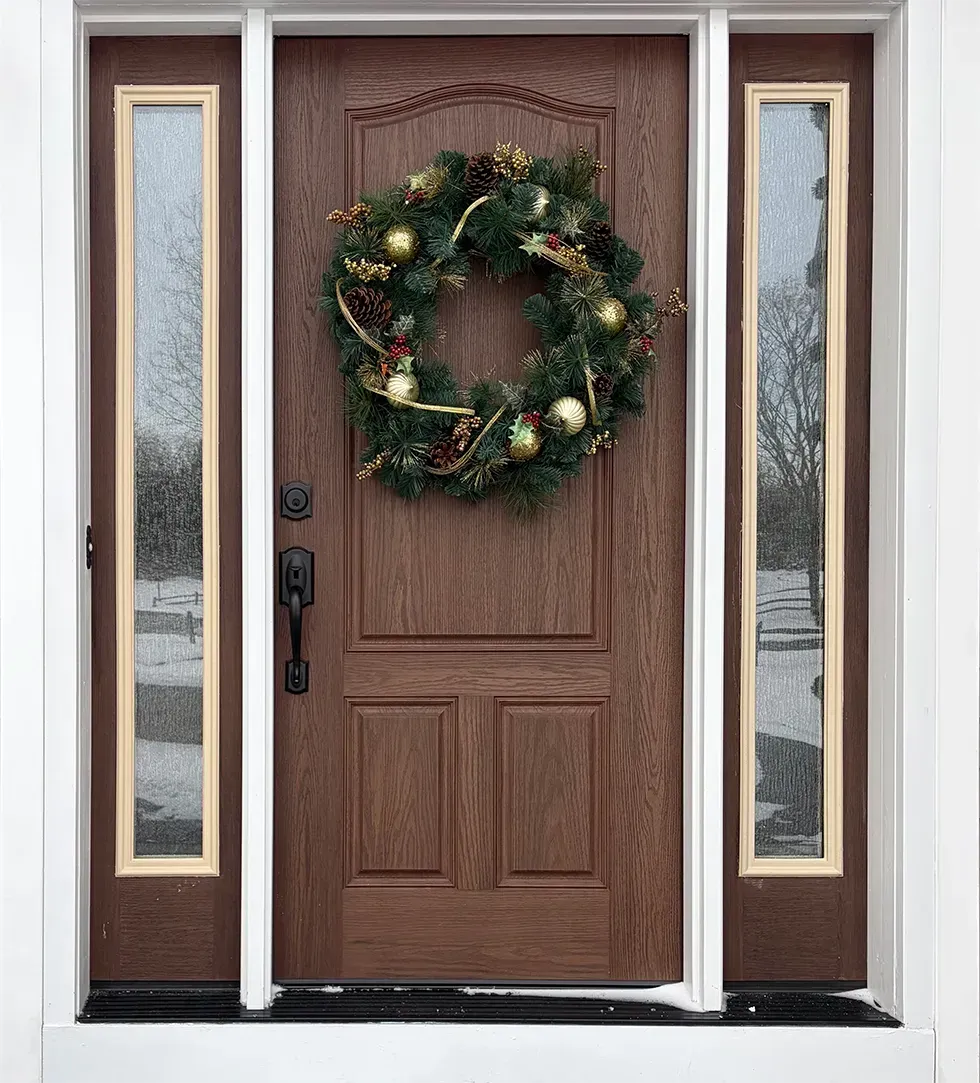 Brown front door with a Christmas wreath, flanked by two sidelights.