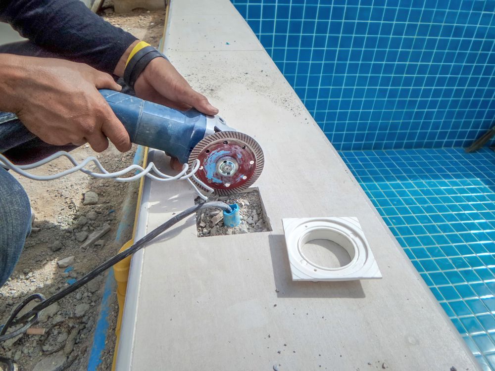 A Man is Using a Grinder to Cut a Hole in a Swimming Pool — NQ Tropical Pools & Renovations in Ingham, QLD