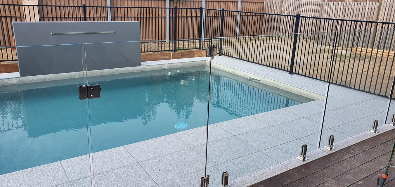 A Large Swimming Pool Surrounded by a Glass Fence and a Wooden Deck — NQ Tropical Pools & Renovations in Cranbrook, QLD
