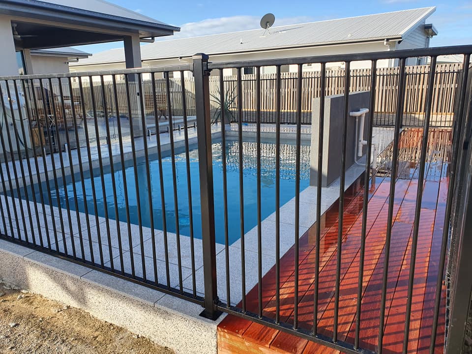 A Fence Around a Swimming Pool With a House in the Background — NQ Tropical Pools & Renovations in Cranbrook, QLD