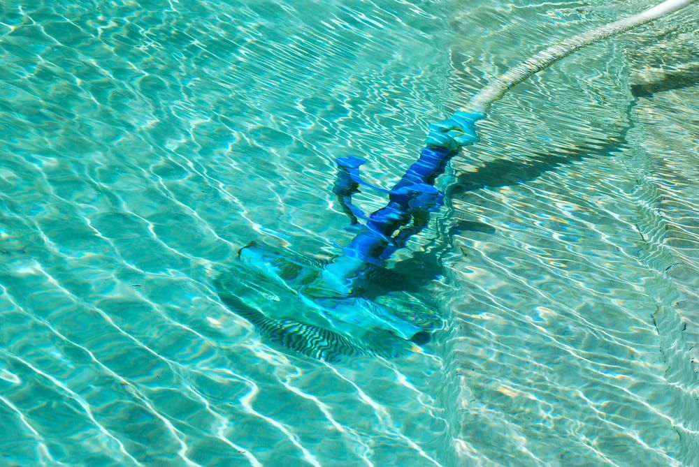A Blue Vacuum Cleaner is Cleaning a Swimming Pool — NQ Tropical Pools & Renovations in Cranbrook, QLD
