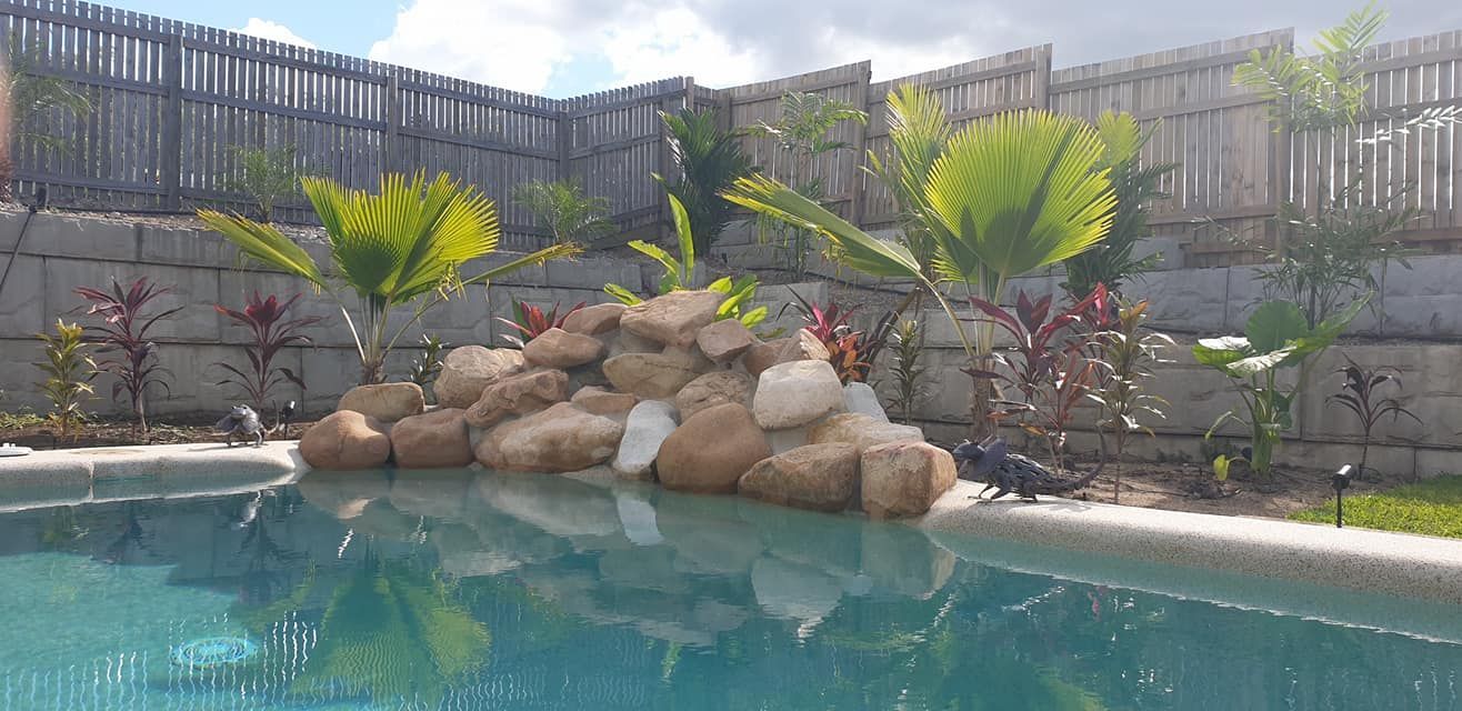 A Swimming Pool With a Waterfall and a Fence in the Background — NQ Tropical Pools & Renovations in Cranbrook, QLD