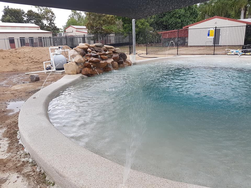 A Large Swimming Pool With a Waterfall in the Middle of It — NQ Tropical Pools & Renovations in Cranbrook, QLD