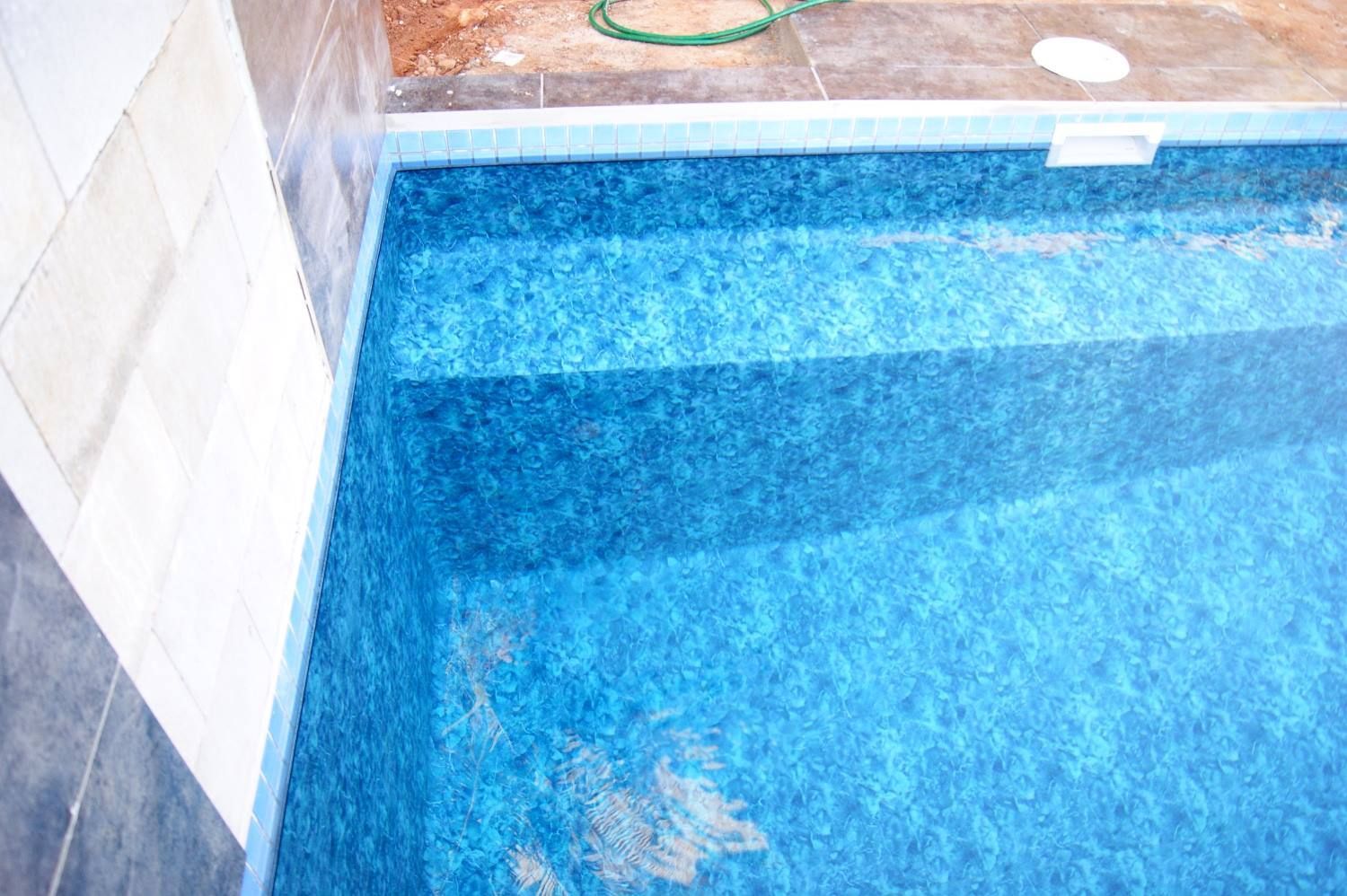 A Blue Swimming Pool With Steps and a Green Hose in the Background — NQ Tropical Pools & Renovations in Burdekin, QLD