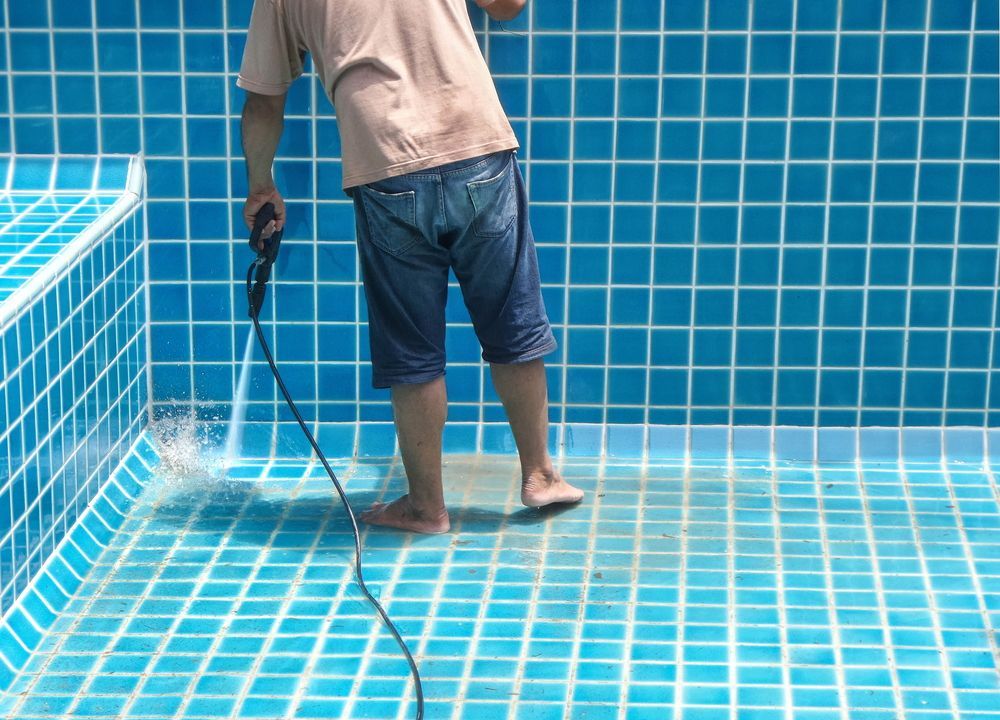 A Man is Cleaning a Swimming Pool With a High Pressure Washer — NQ Tropical Pools & Renovations in Bowen, QLD