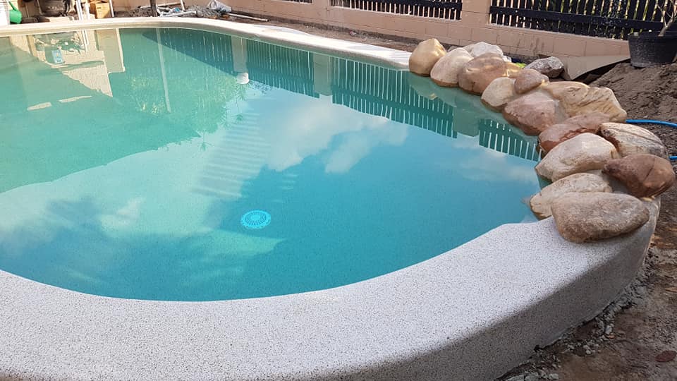 A Large Swimming Pool Surrounded by Rocks and a Fence — NQ Tropical Pools & Renovations in Cranbrook, QLD