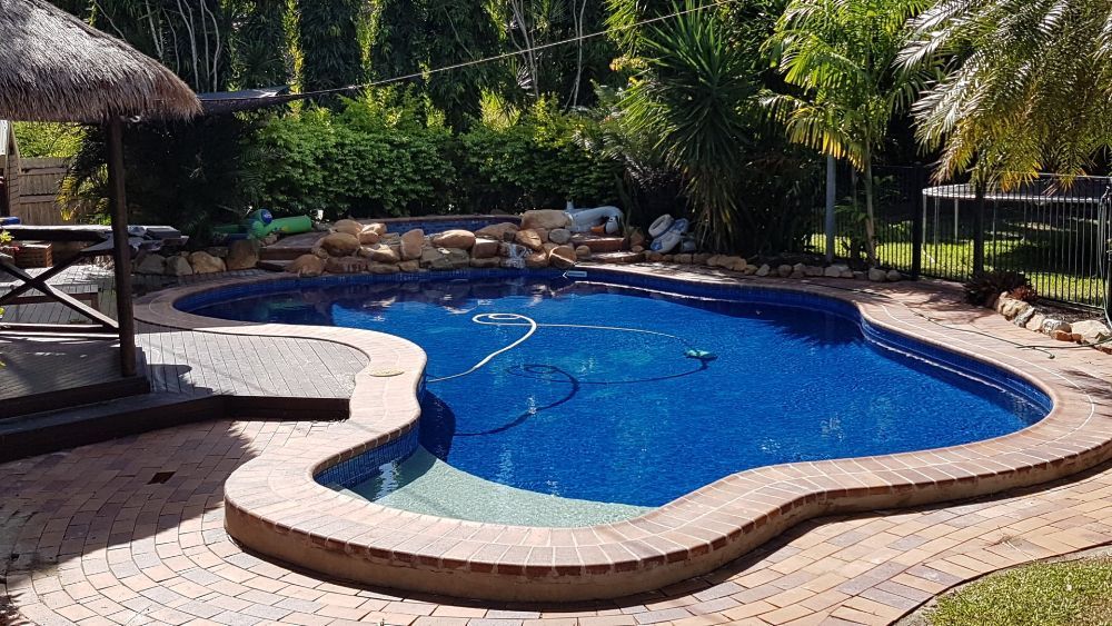 A Large Swimming Pool With a Thatched Umbrella in the Background — NQ Tropical Pools & Renovations in Cranbrook, QLD