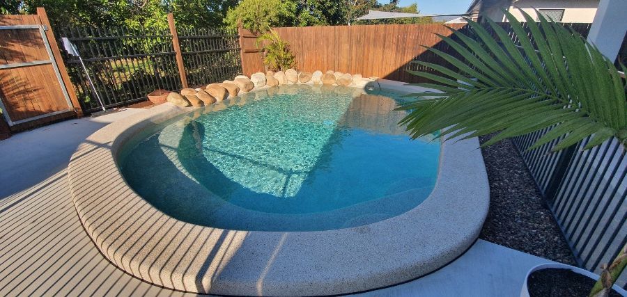 A Small Swimming Pool is Surrounded by a Wooden Deck and a Palm Tree — NQ Tropical Pools & Renovations in Cranbrook, QLD