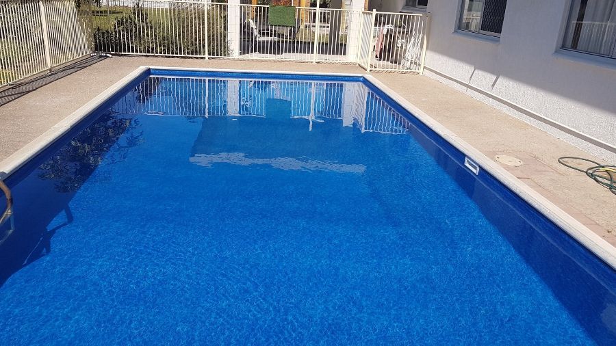 A Large Blue Swimming Pool With a White Fence Around It — NQ Tropical Pools & Renovations in Cranbrook, QLD