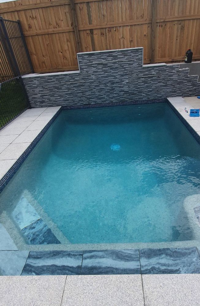 A Large Swimming Pool With a Wooden Fence in the Background — NQ Tropical Pools & Renovations in Cranbrook, QLD