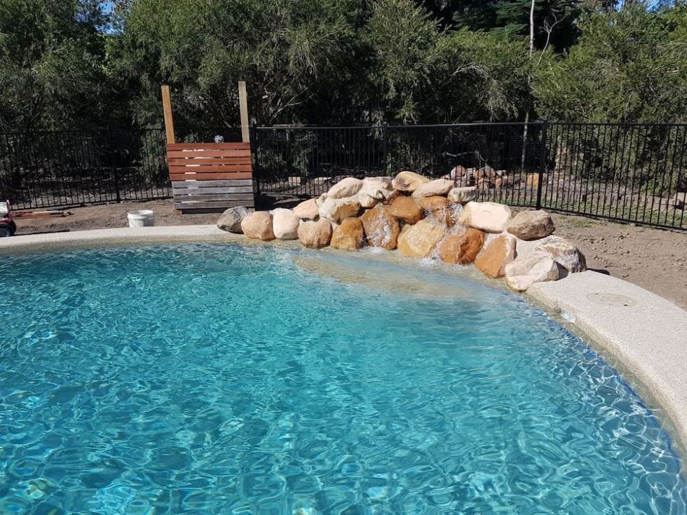 A Large Swimming Pool Surrounded by Rocks and Trees — NQ Tropical Pools & Renovations in Cranbrook, QLD