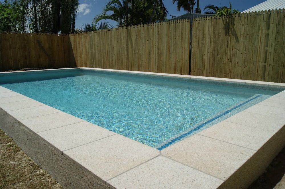 a Swimming Pool With a Wooden Fence Surrounding It — NQ Tropical Pools & Renovations in Cranbrook, QLD
