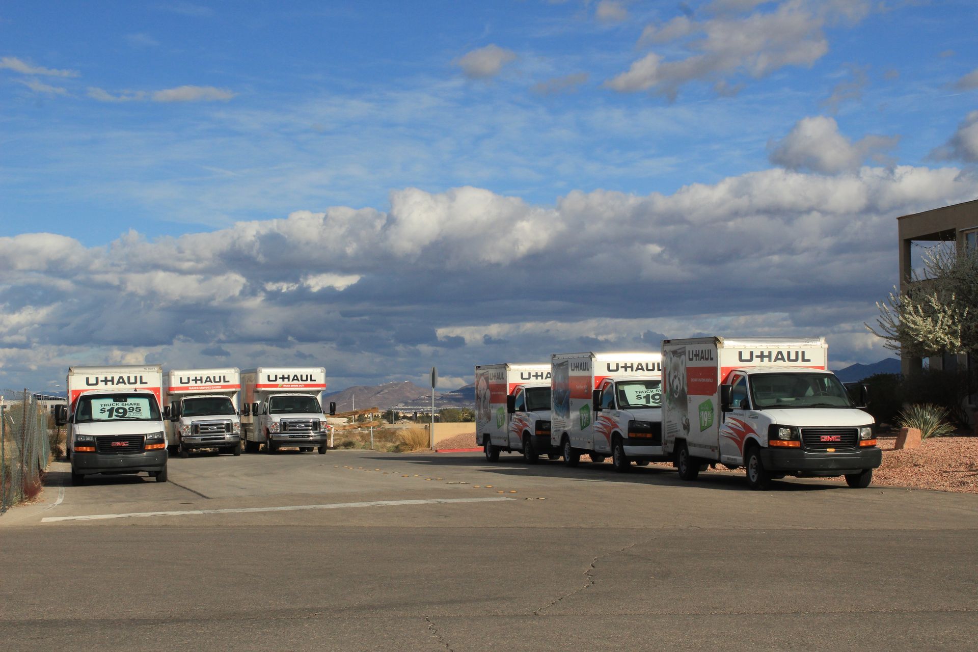 Several U-Haul trucks parked outdoors on a sunny day with scattered clouds.