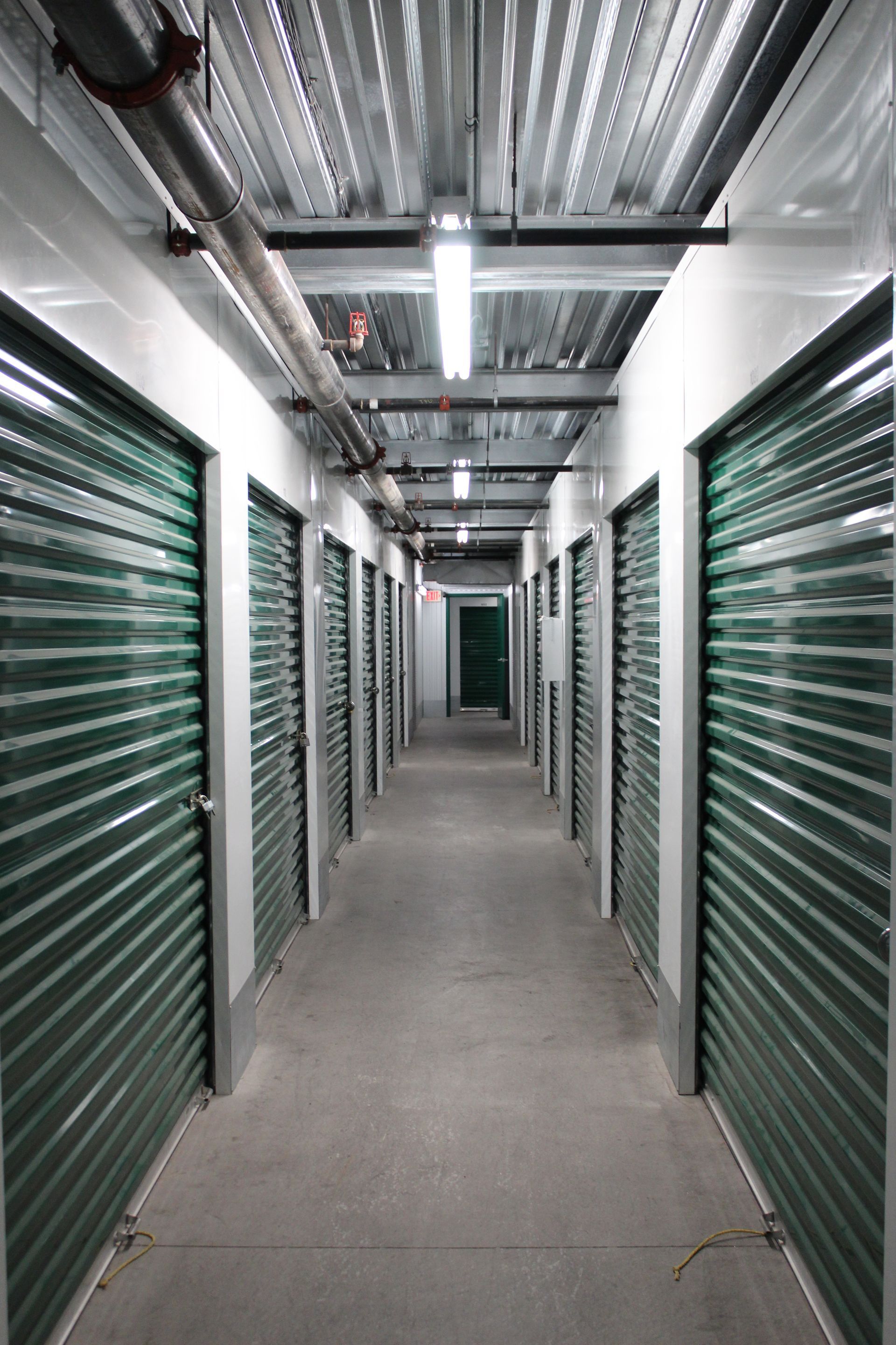 Hallway of green storage units with a concrete floor and a metal ceiling.