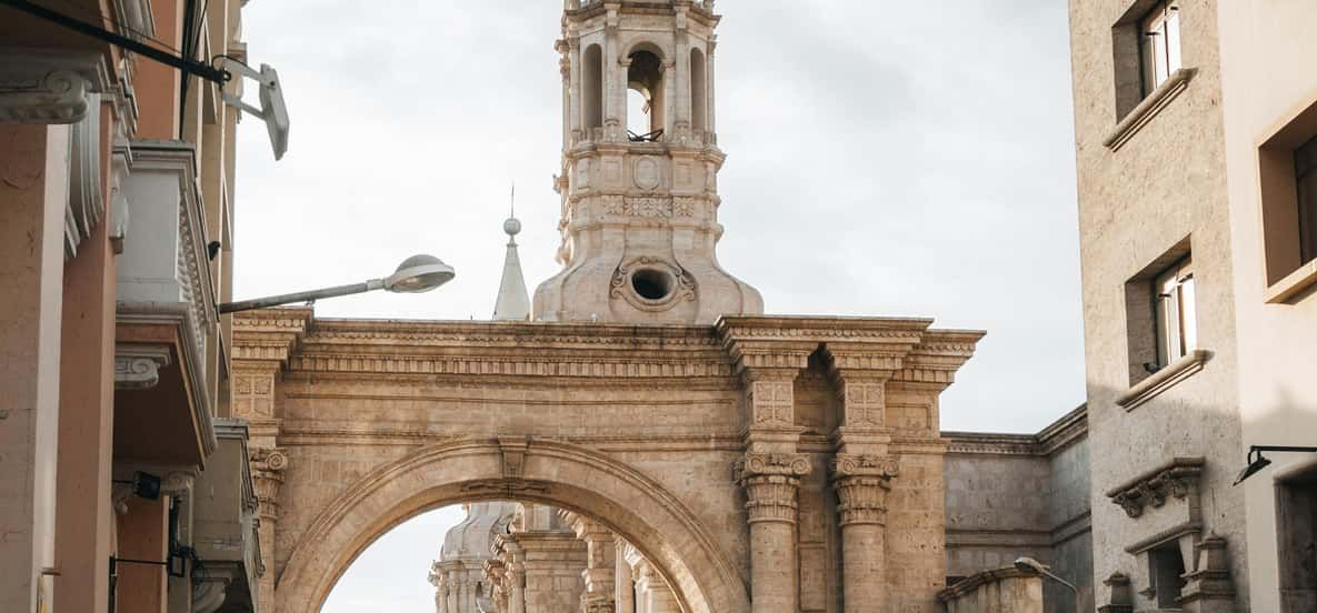 Arco de piedra que conduce a la torre de una iglesia en una calle estrecha entre edificios.
