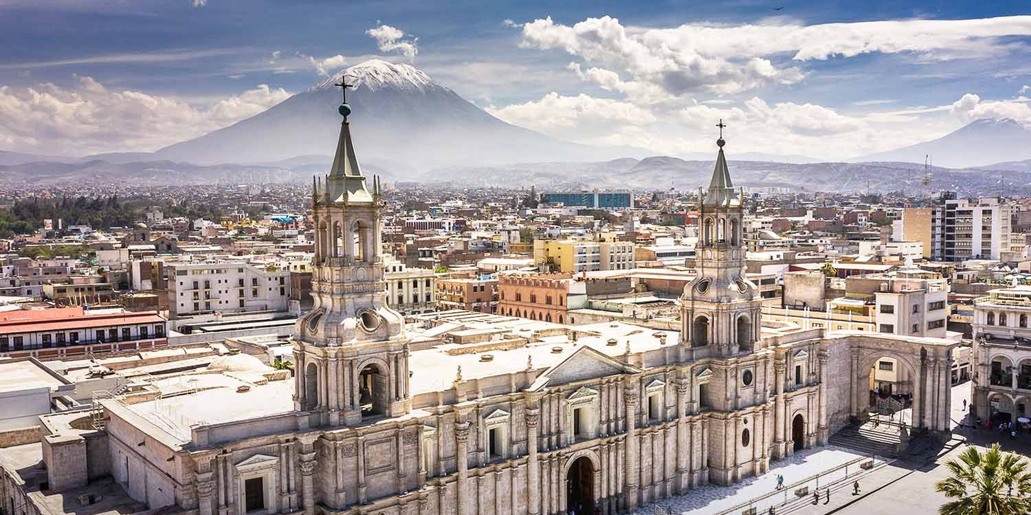 Vista panorámica de la ciudad con una gran catedral y un volcán nevado al fondo, bajo un cielo despejado.