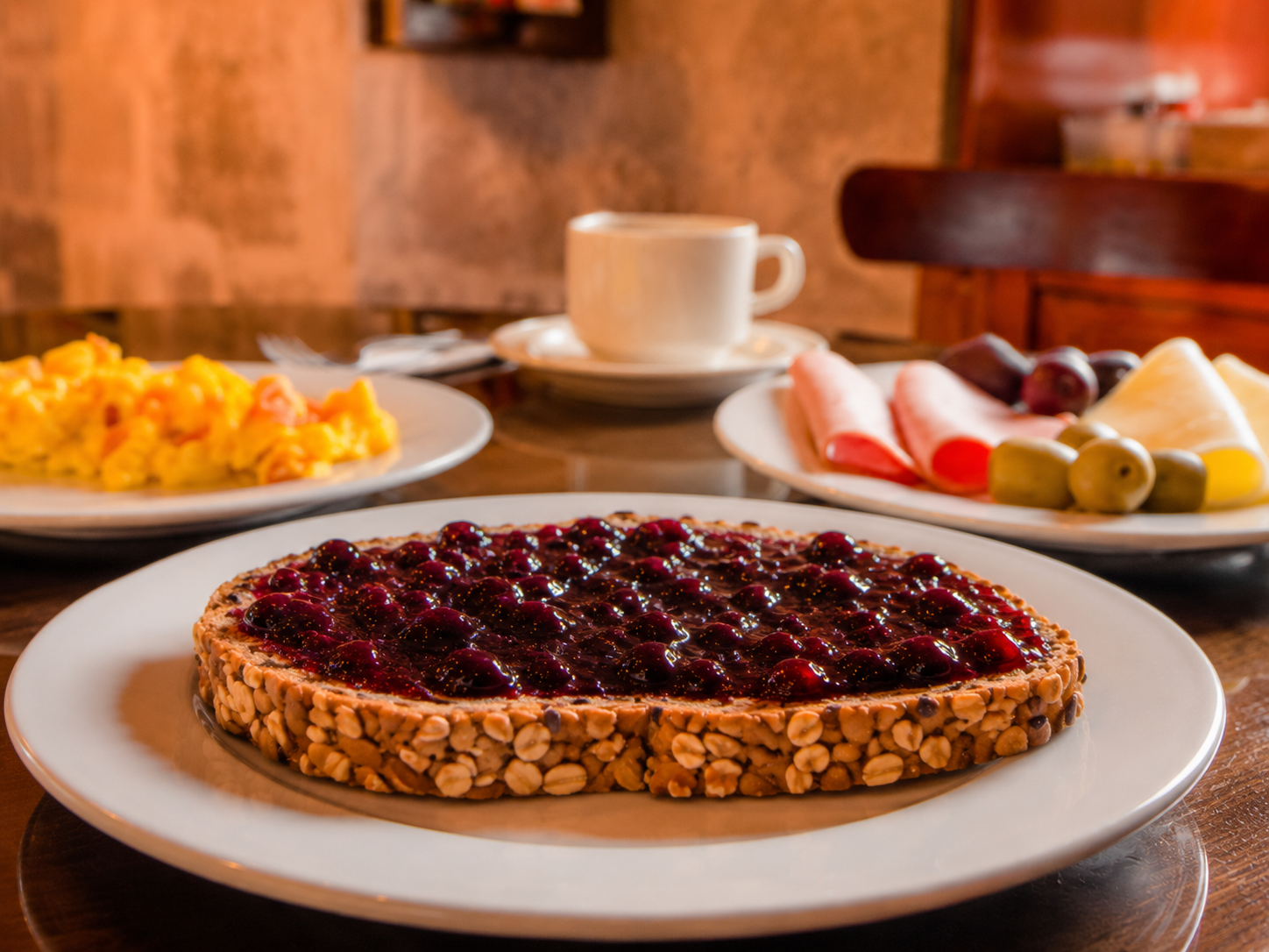 Tarta de frutos rojos sobre una mesa con café, huevos revueltos y fruta en un acogedor ambiente de desayuno de cafetería.