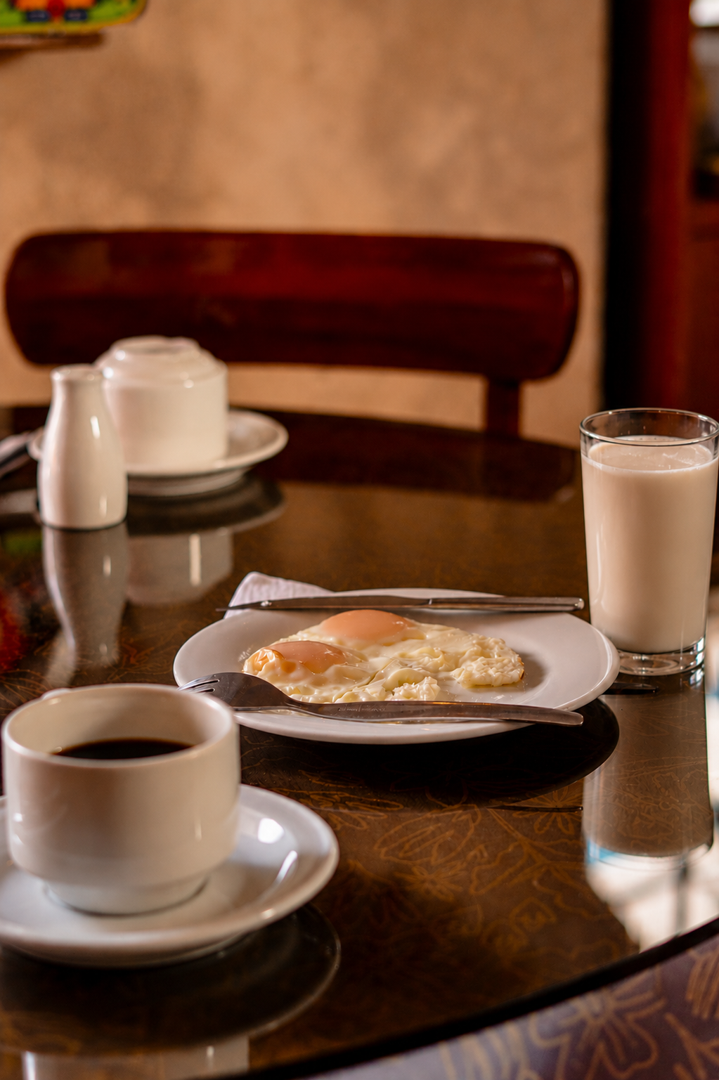 Mesa de desayuno con café, leche, bollería y un vaso de zumo sobre una mesa de madera oscura.