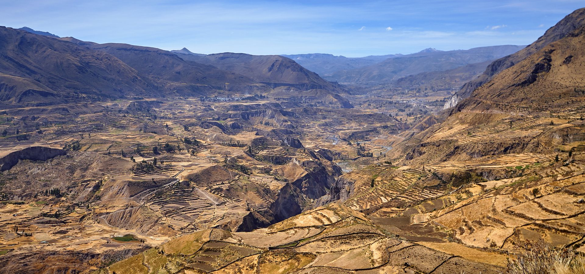 Amplio valle montañoso árido con colinas rocosas, vegetación escasa y un horizonte azul lejano.