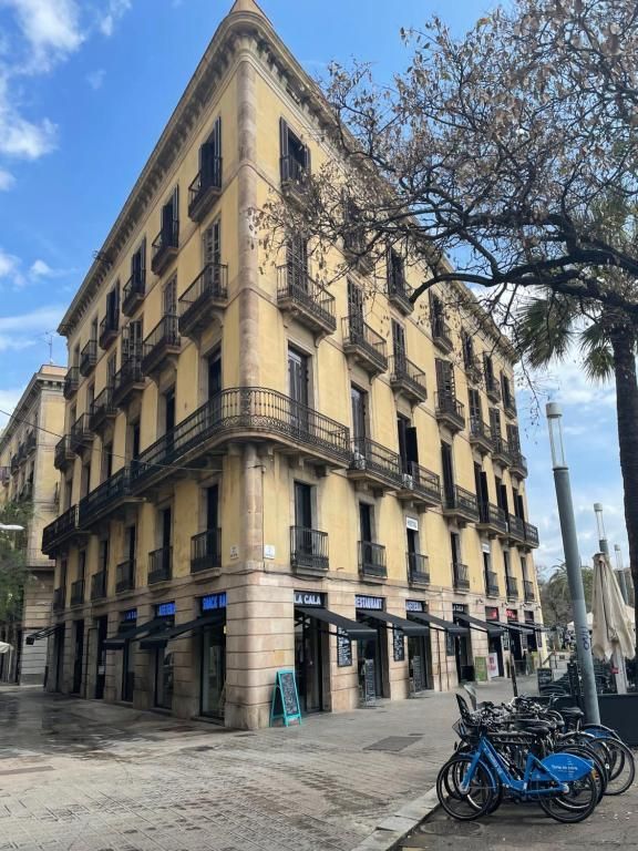Un edificio esquinero de varios pisos de color amarillo en Barcelona, ​​con balcones oscuros, tiendas en la planta baja.