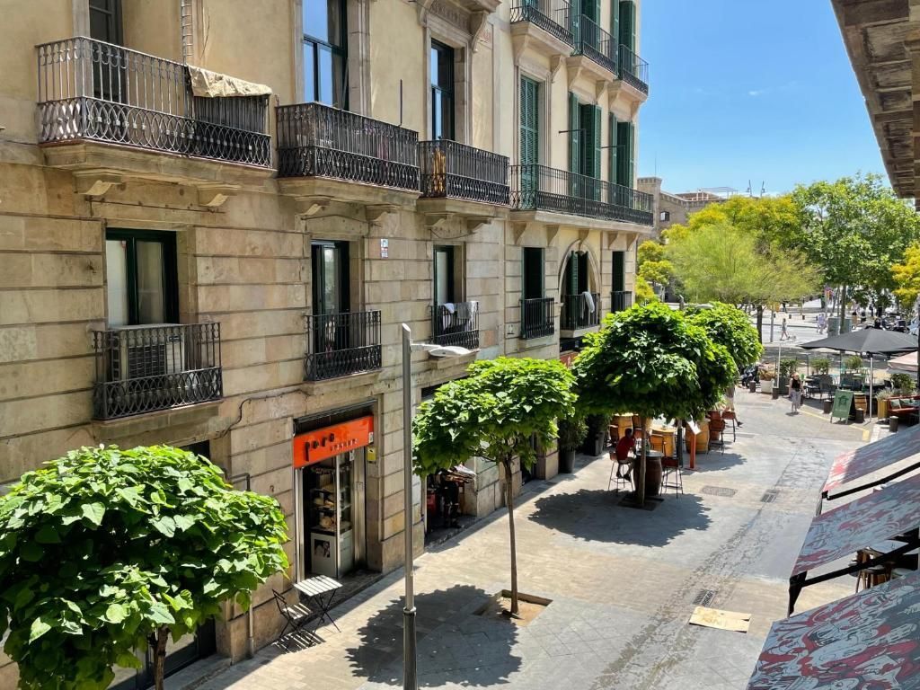 Una escena callejera europea iluminada por el sol con edificios de piedra con balcones, árboles verdes.