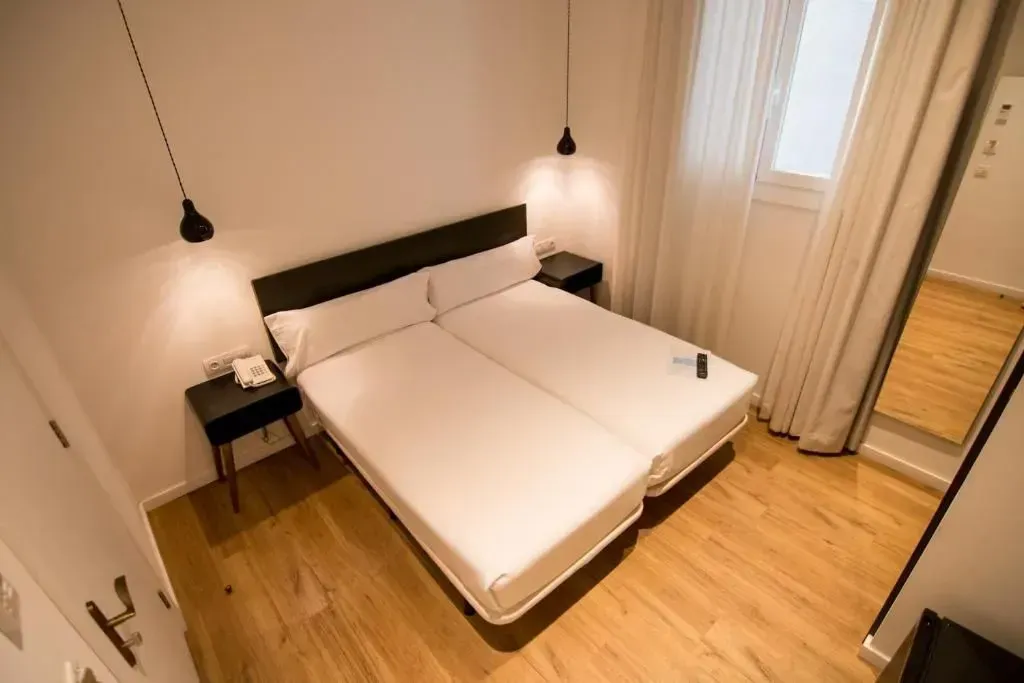 Un dormitorio de hotel moderno con dos camas individuales una al lado de la otra, pisos de madera, mesitas de noche.