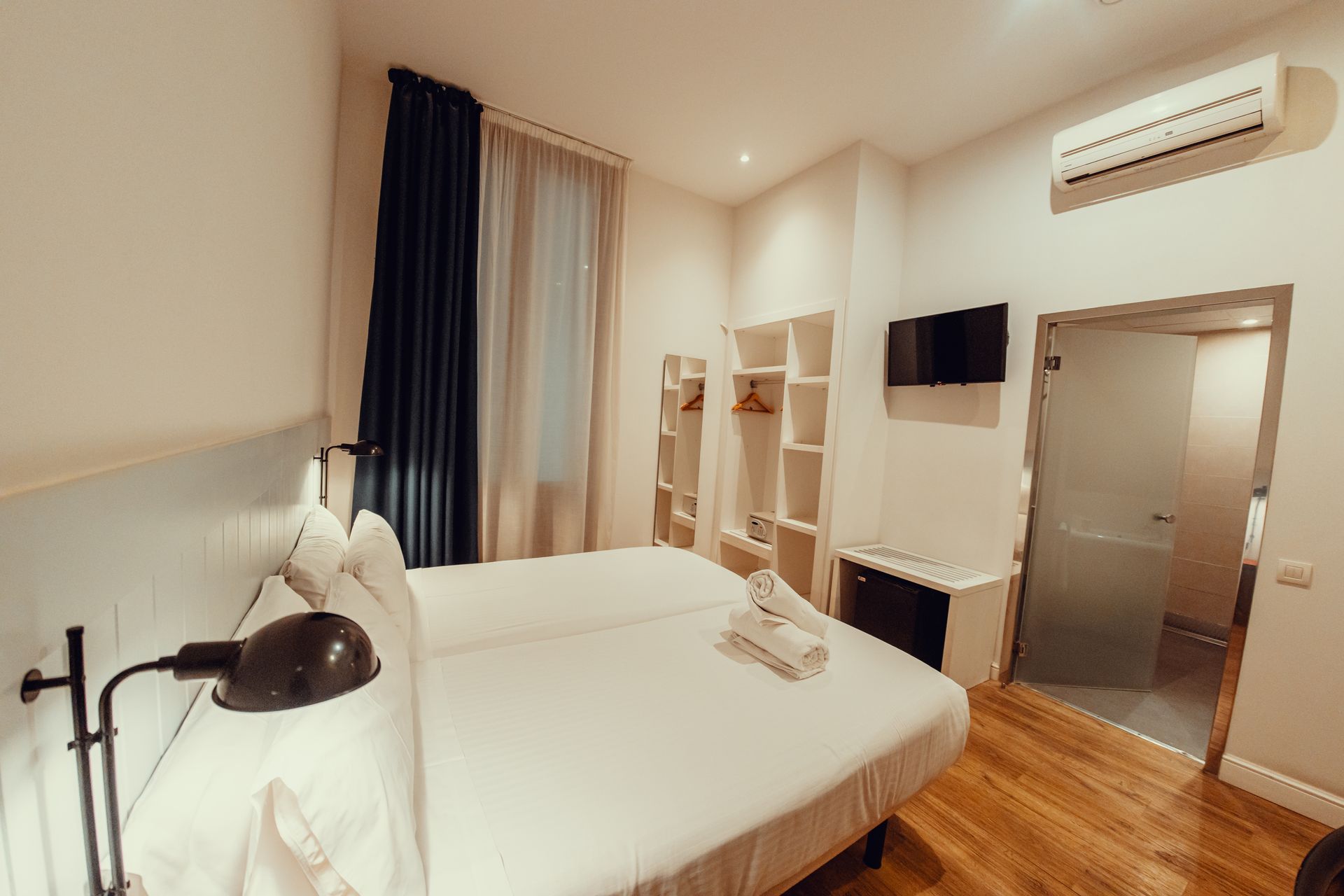 Habitación de hotel luminosa con una cama grande, cortinas en la ventana, escritorio y puerta del baño abierta hacia un lado.