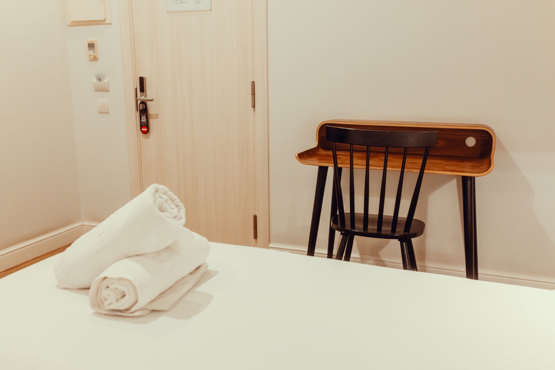 Habitación de hotel con una cama bien hecha, toallas dobladas, una silla y un escritorio junto a la puerta.