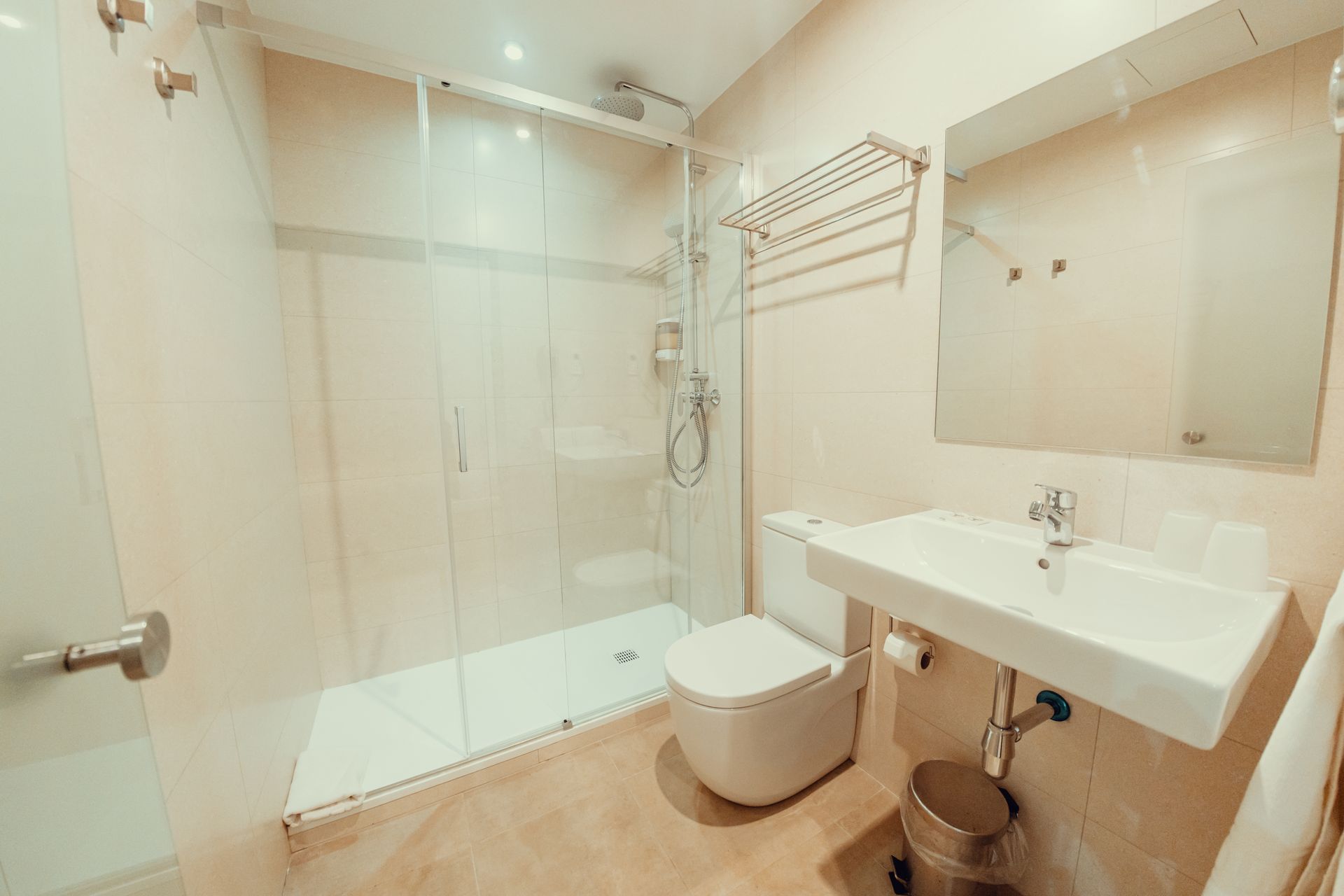 Baño moderno y luminoso con ducha de cristal, inodoro y lavabo mural con espejo.
