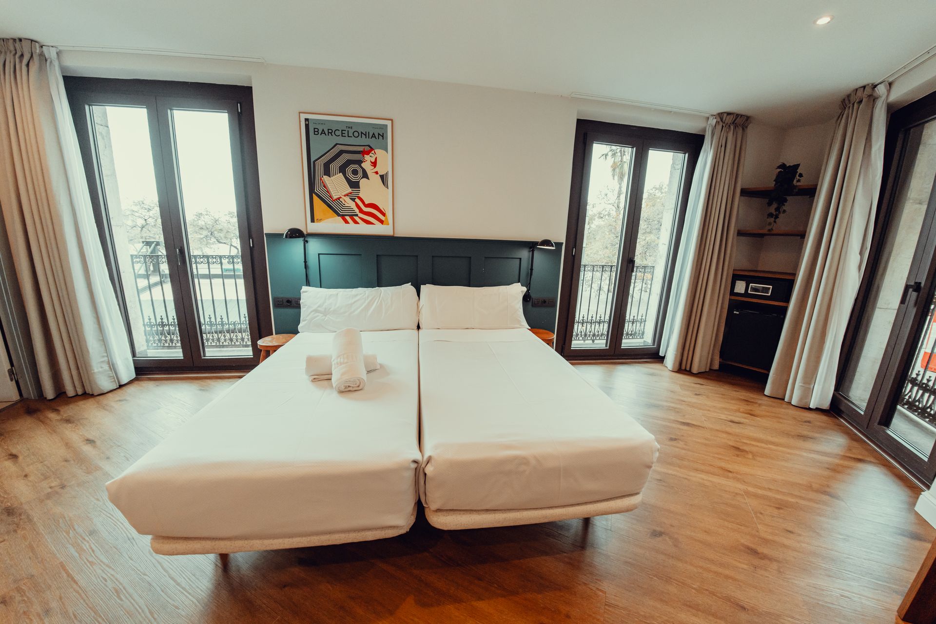 Habitación luminosa con dos camas individuales, suelos de madera y puertas francesas que dan a un balcón.
