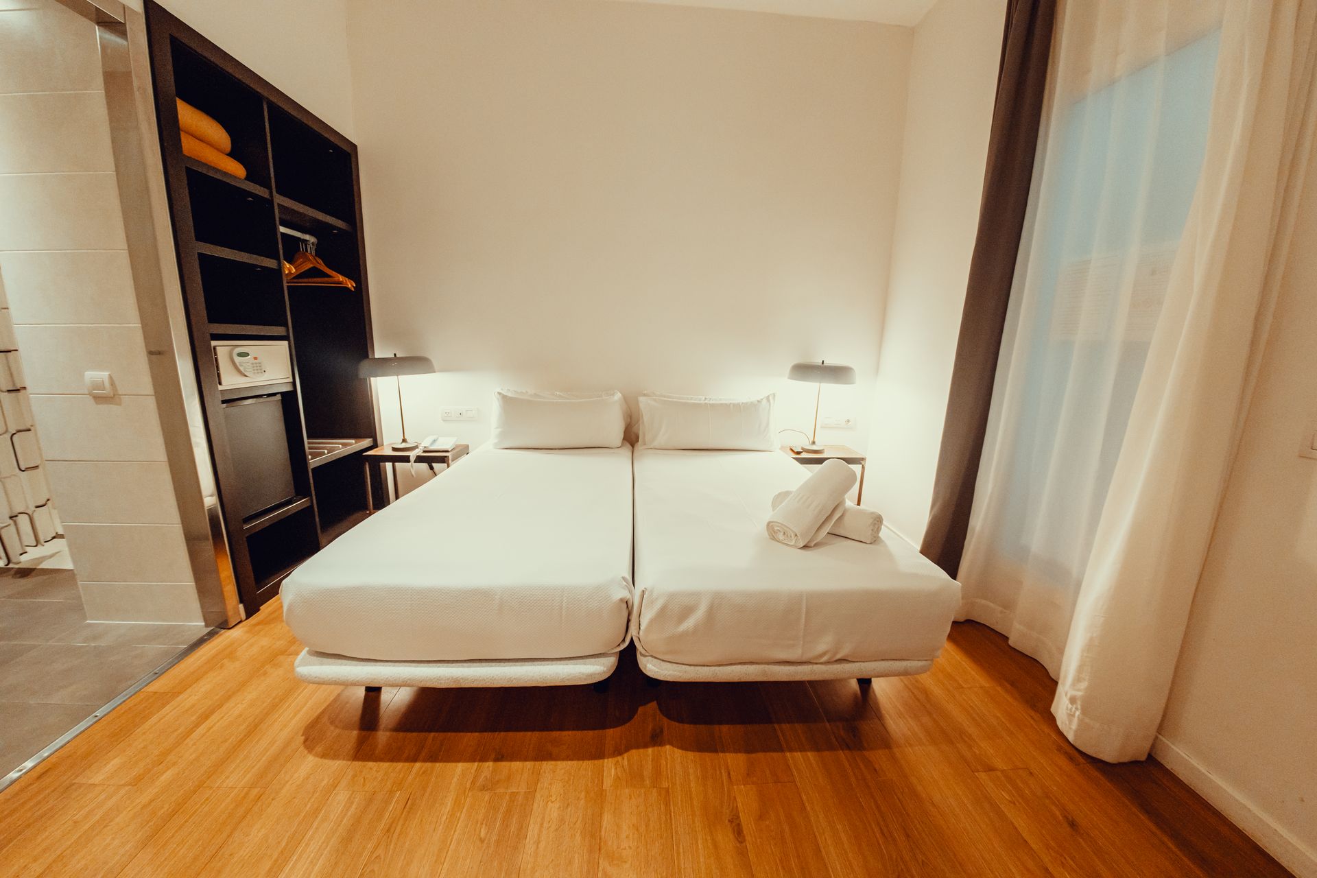 Habitación moderna con dos camas individuales, suelo de madera cálida y cortinas transparentes.