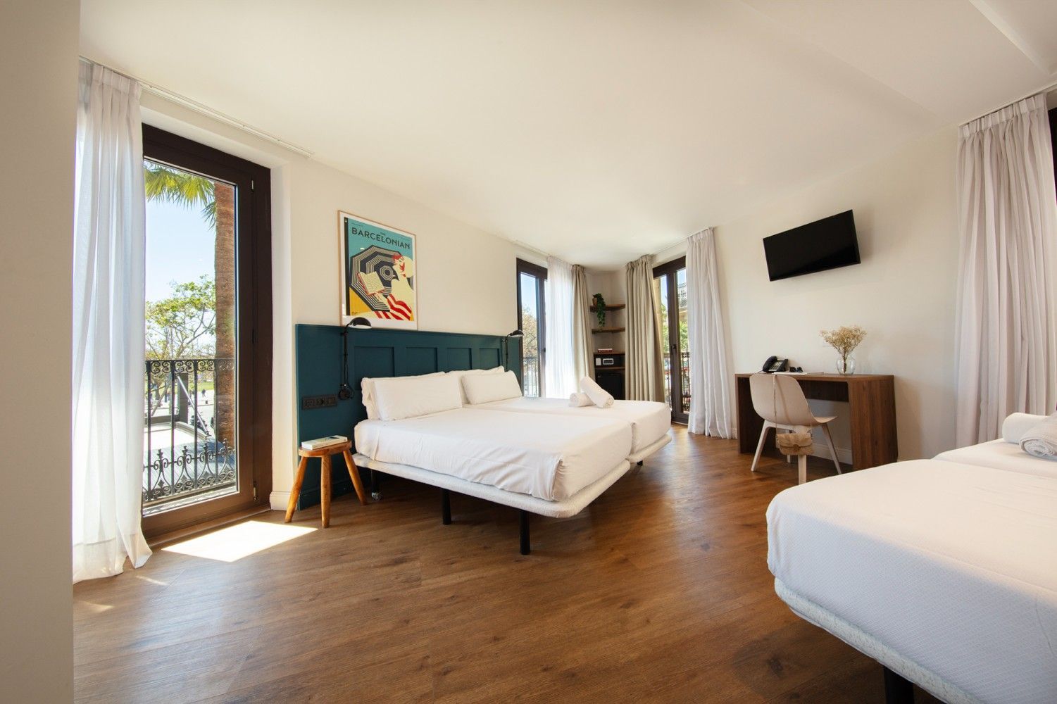 Una habitación de hotel con dos camas, pisos de madera, cortinas blancas, un escritorio con una silla.