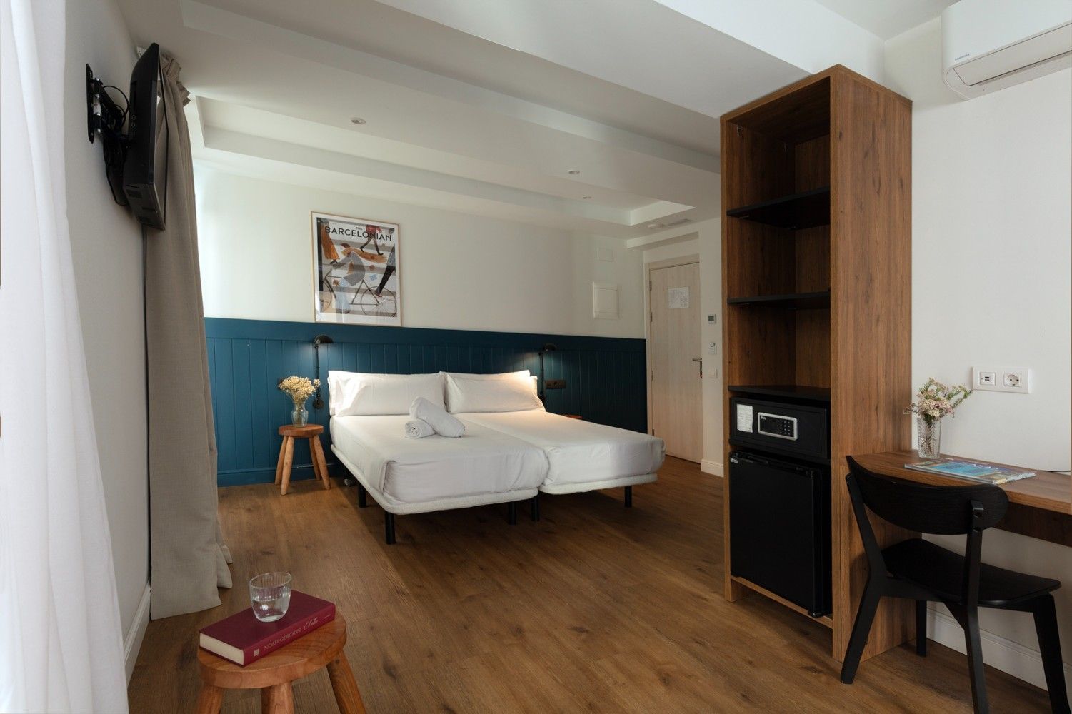 Una moderna habitación de hotel con dos camas individuales blancas contra una pared con paneles azules, una estantería.