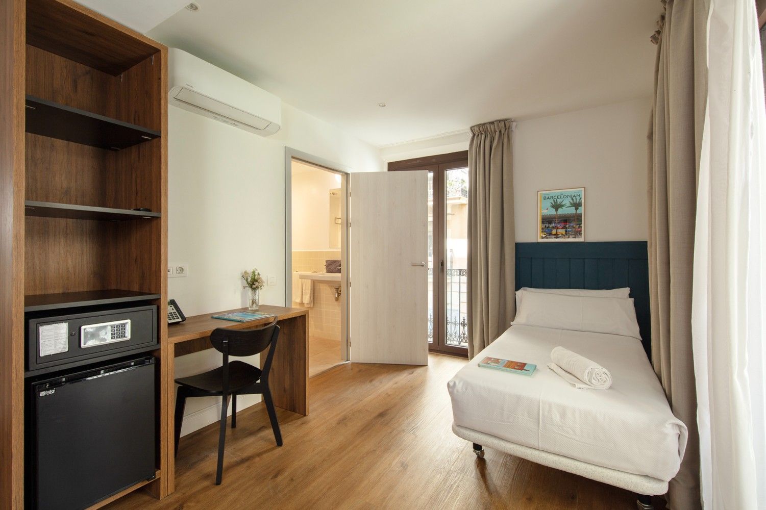 Una moderna habitación de hotel con una cama individual, un escritorio con silla y un armario abierto.