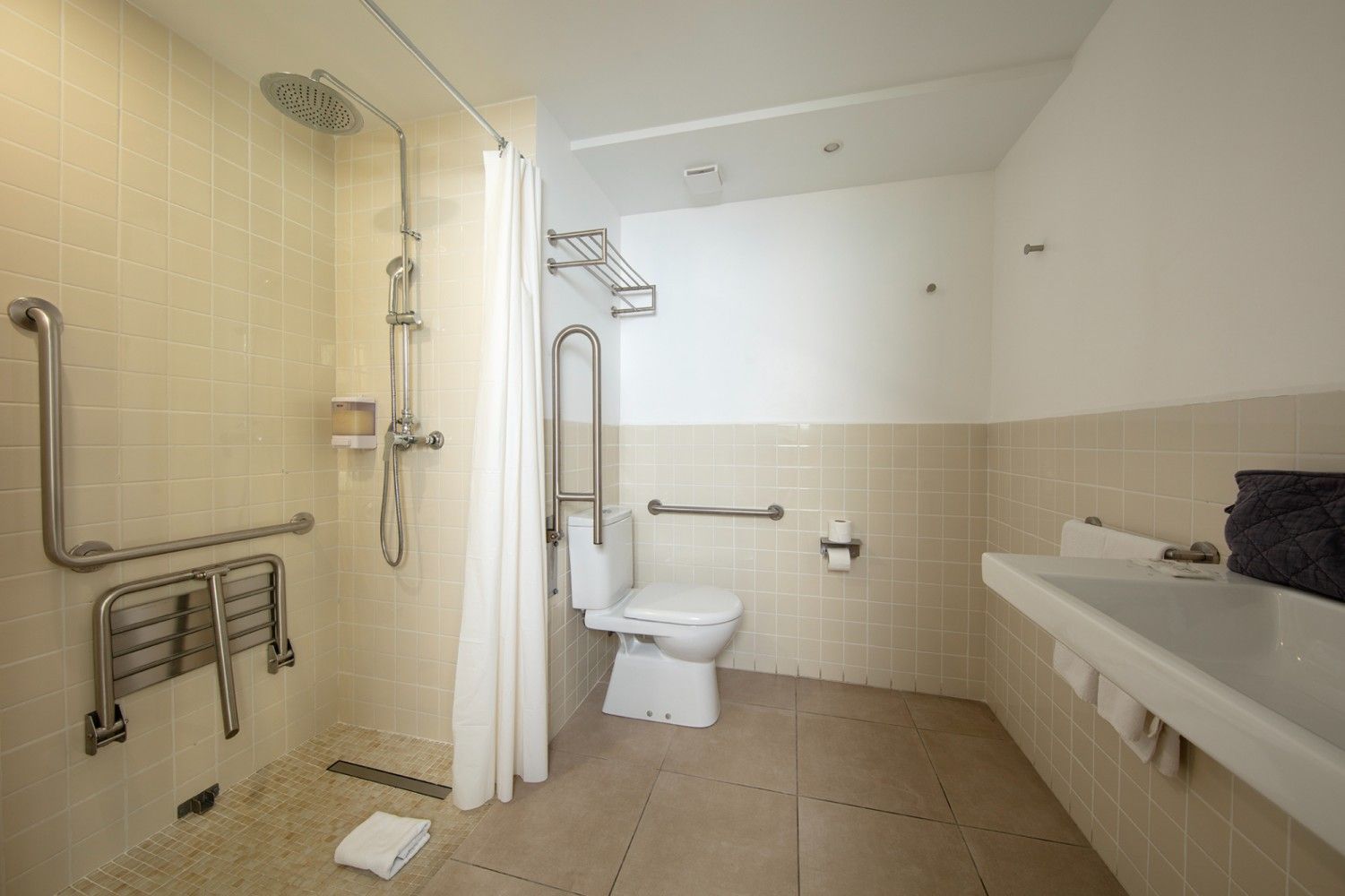 Baño accesible con ducha adaptada para personas en silla de ruedas con asiento abatible, barras de apoyo, inodoro.