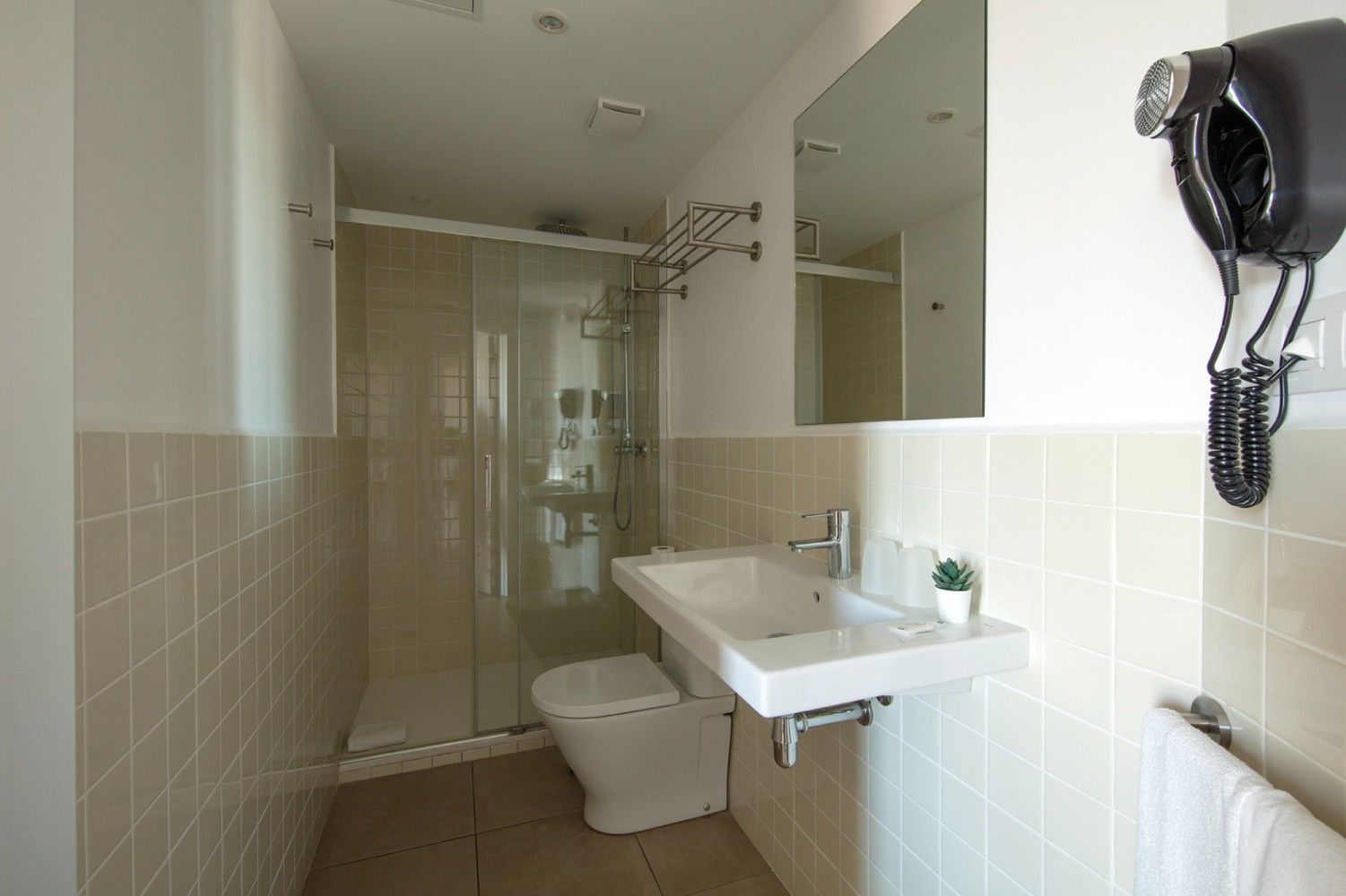 Un moderno baño con azulejos que cuenta con lavabo, espejo, secador de pelo de pared.