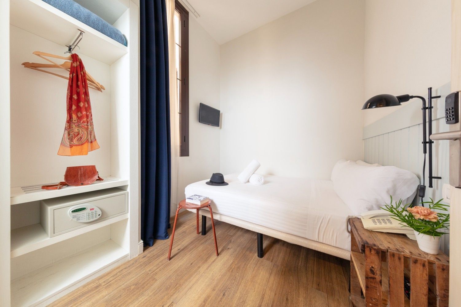 Una habitación de hotel pequeña y ordenada con una cama individual, una mesita de noche de madera y un armario .